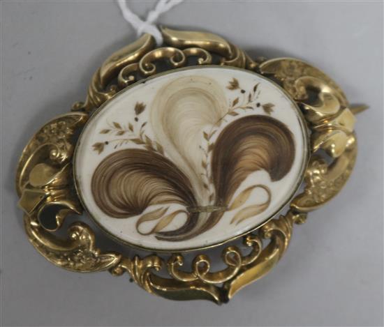 A Victorian pinchbeck brooch with central oval glazed hairwork panel in pierced and scrolled mount, 61mm.